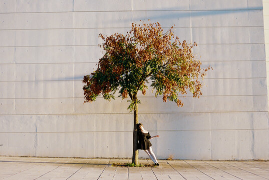 Dancer leaning back on tree in city sunlight