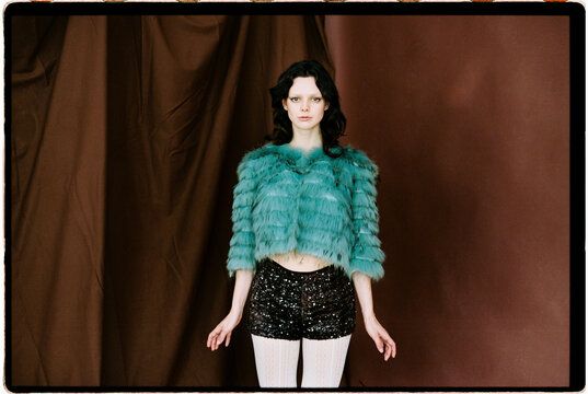 Woman posing indoors wearing teal fur and sequins