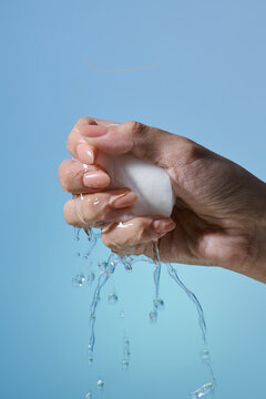 Hand squeezing water from a white sponge against a light blue