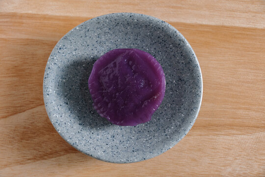 Top view Indonesian kue talam ubi on small grey plate over wooden board. Traditional sweet dessert made from purple yam and coconut for Asian food concept.