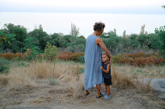 A woman hugs her son on a slope by the sea