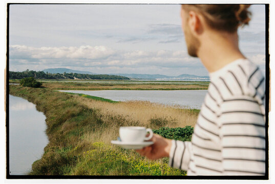 A person drinking coffee on a rooftop with a river view
