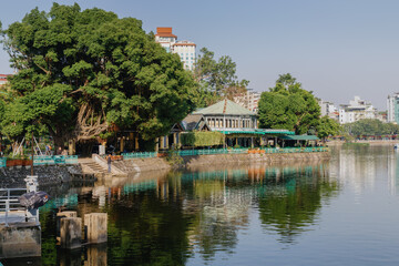 Obraz premium A serene view of Truc Bach Lake in Hanoi, Vietnam, where a local is fishing. The lake reflects the surrounding trees and buildings, creating a peaceful urban scene.