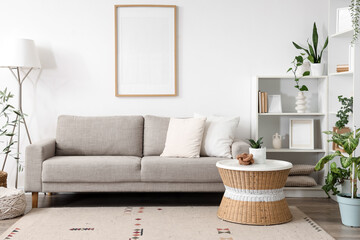 Fototapeta premium Interior of light living room with sofa, blank frame and green plants