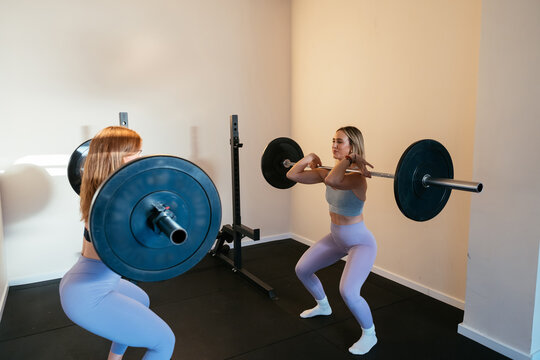 Women weightlifting barbells doing squats in gym