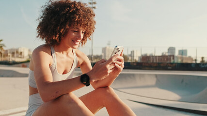 Young Woman Using Phone At Sunny Skatepark