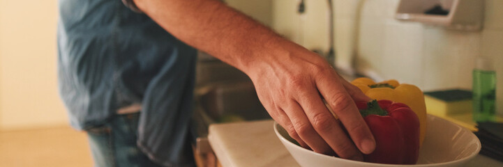 Obraz premium Close-up of the hands of guy dressed in denim shirt washing vegetables in the kitchen in the apartment, vegetables in the foreground. Panoramic