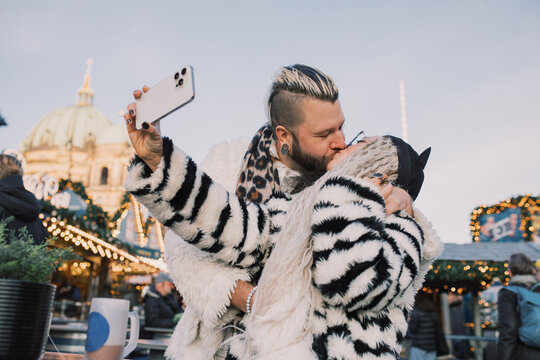 Couple Takes Selfie While Sharing a Kiss in Festive Setting
