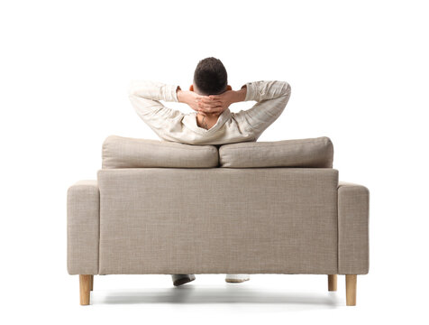 Young man sitting on grey sofa against white background, back view