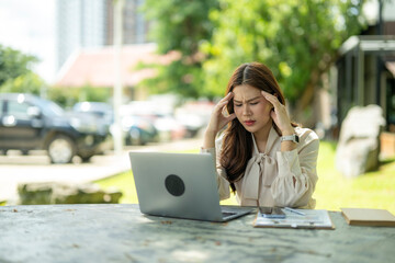 Fototapeta premium Stressed businesswoman suffering headache working on laptop outdoors