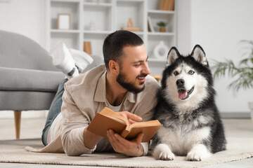Handsome young man lying on floor and reading book with cute husky dog at home © Pixel-Shot