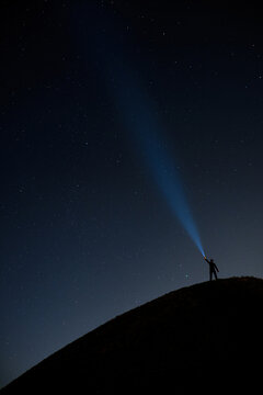 Person with flashlight under a starry night sky