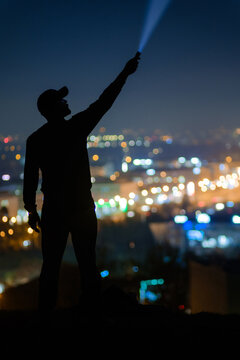 Silhouette with flashlight above the glowing city at night