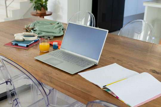 Silver laptop sitting open on wooden dining table with lined notebook and yellow pencil nearby