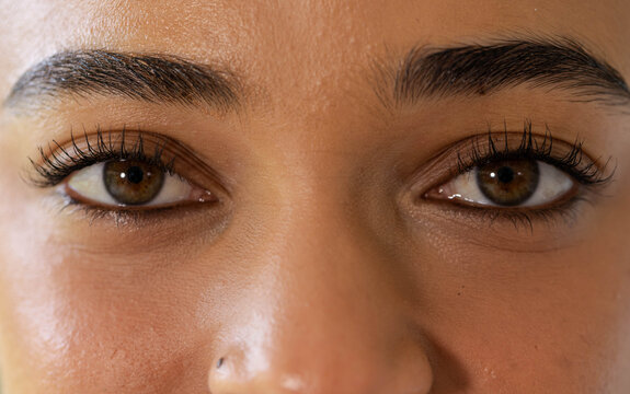 Metallic nose stud catching soft studio light on warm textured skin, with mascara-lined eyes