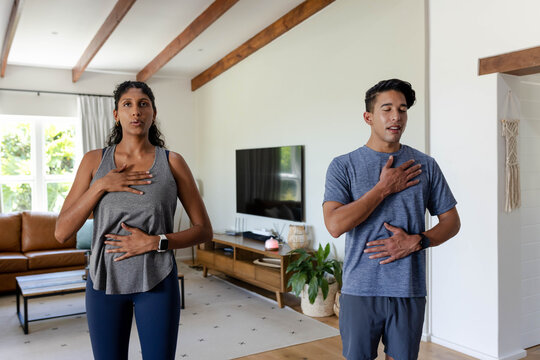 African American couple practicing breathwork in living room wearing athletic wear near TV