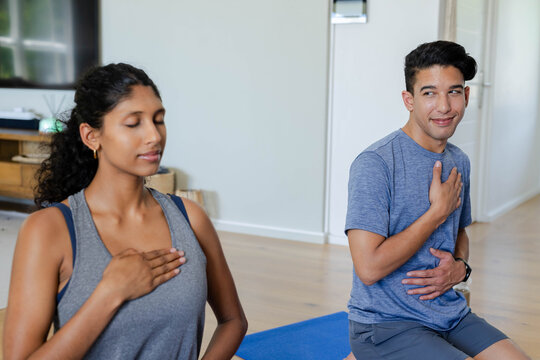 Couple practicing breathing exercises sitting on blue yoga mats in living room wearing sportswear