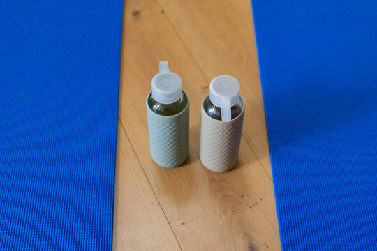 Two glass water bottles are standing on wooden plank between bright blue mats, showing sleeves
