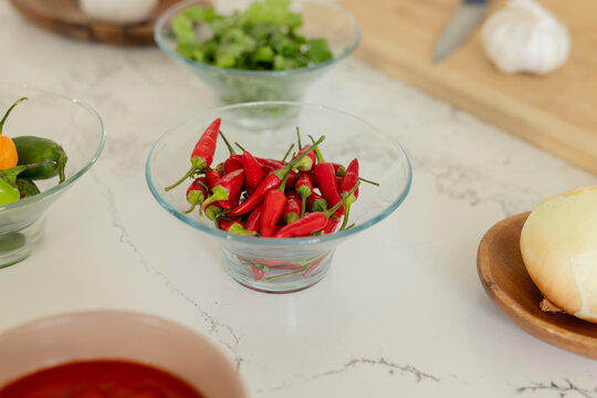 Clear glass bowl holding red chilies sitting on marble countertop, with garlic and onion nearby