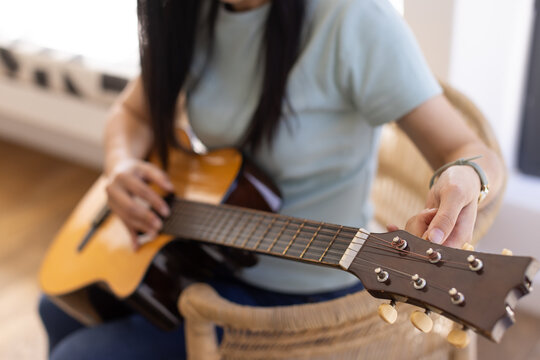 Acoustic guitar neck and headstock are being adjusted on wicker chair near bright window