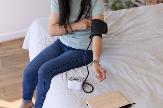 Digital blood pressure cuff is being adjusted on arm on bed near wooden notebook and plant