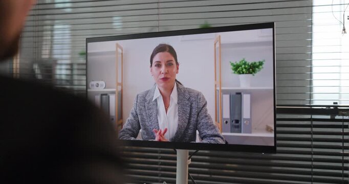 Woman on video call in office meeting. She is talking in an online business chat on a large screen, suited for remote support and interviews. Clear concept of remote business communication.