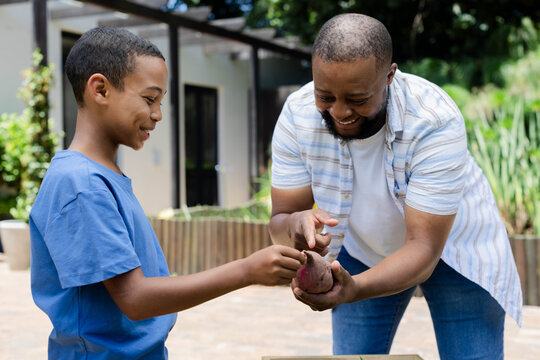 African American man showing adolescent boy sweet potato on patio in striped shirt and blue tee