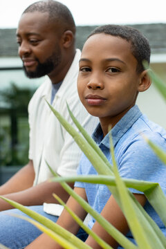 African American dad, teenage son sitting on porch amid aloe leaves, wearing blue polo and shirt