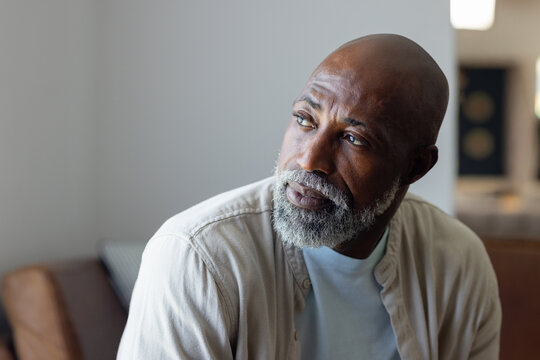 Senior African American man sitting on sofa in living room, gazing right, wearing light beige shirt