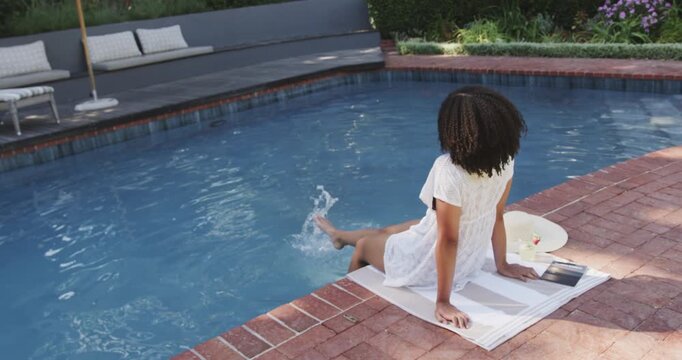 Back-facing figure is lowering legs into pool at brick coping, then is kicking to cool feet