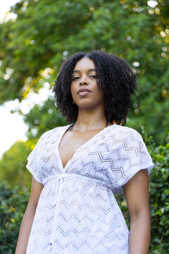 African American woman standing and posing in garden with bokeh leaves in white lace dress