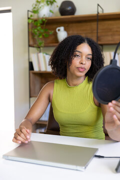 African American woman sitting at desk wearing lime green top adjusting pop filter near shut laptop