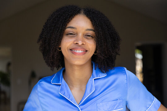 African American woman smiling, standing in entry wearing blue satin top, gold hoops, doorway