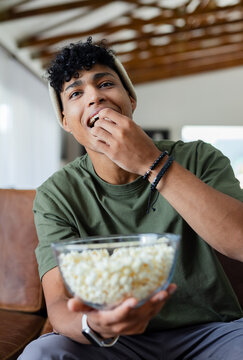 African American man sitting on leather couch at home wearing olive tee holding popcorn bowl