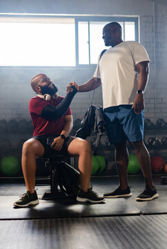 Two adult African American men greeting, clasping hands at gym bench holding smartphone, duffel