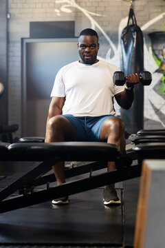 African American man wearing workout clothes lifting hex dumbbell on adjustable bench at gym