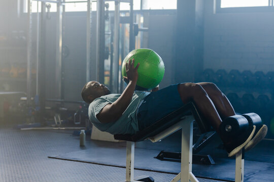 Bright green medicine ball is resting on decline bench in weight room with diffused daylight haze