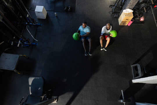 Two African men in sportswear doing core exercise with green medicine balls on gym floor