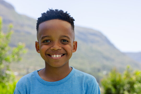 African male child smiling and facing camera in valley with shrubs and hills, wearing blue t-shirt
