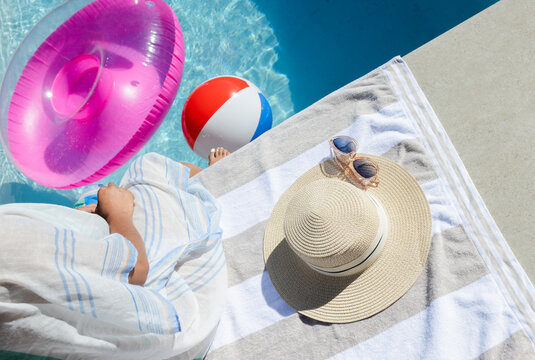African American woman wearing striped cover-up sitting at pool edge, feet in pool, pink ring