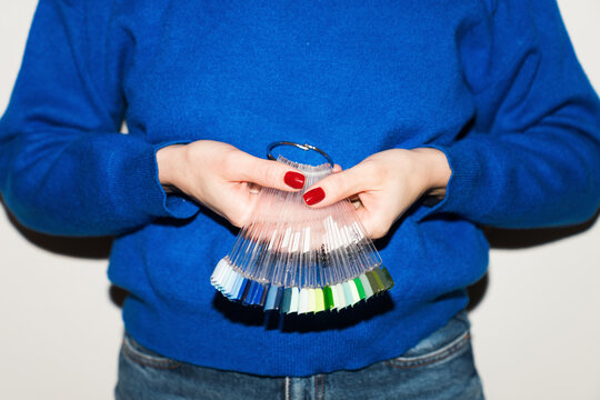 Hands hold a collection of nail polish samples in a bright room.