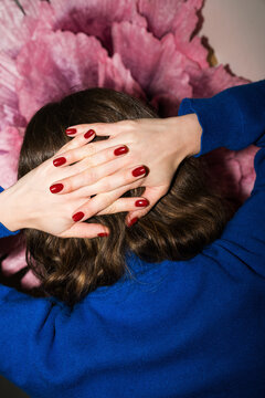 Woman with red nails sits against pink flower background