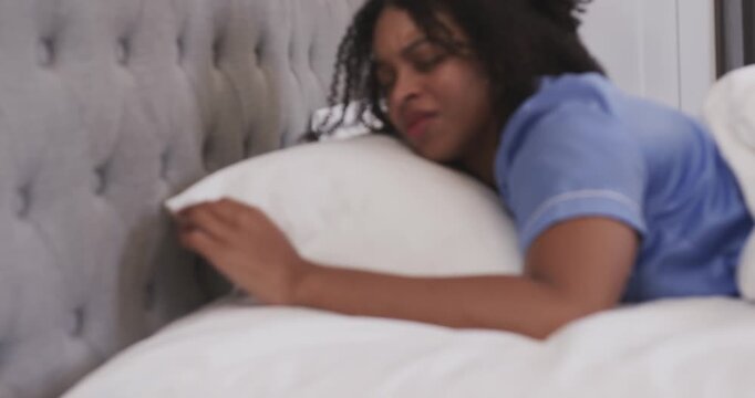 African American woman waking in bed to buzzing cell reaching table silencing cell resting in pjs