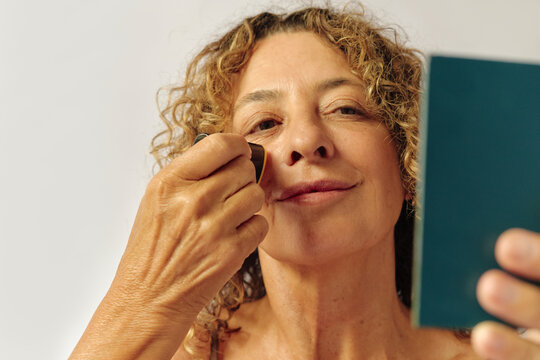 Woman applying skincare product in her face in the mirror