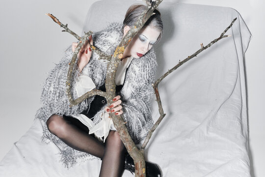 Bizarre Fashion Portrait of Woman in Fur Coat with Tree Branch