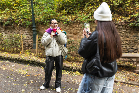 Two young women having fun taking photos in autumn park