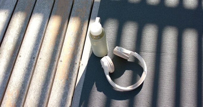Sunlight is shifting and casting striped shadows over mat, bottle, headphones as sun is moving