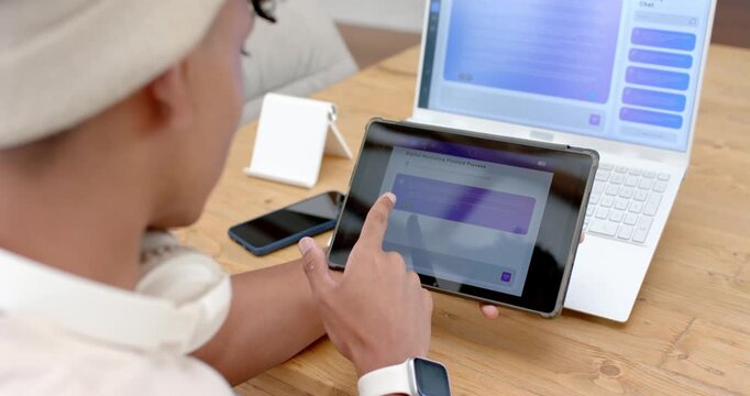 African American man glancing at tablet, tapping purple tile while doing work on laptop, copy space