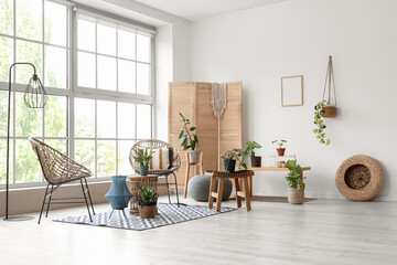 Fototapeta premium Interior of light room with wicker armchairs, tables and green plants
