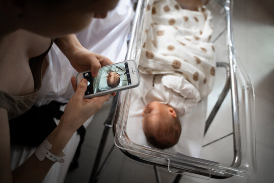 Mother photographing newborn baby in hospital bassinet